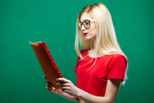 Vista laterale di grave studentessa in occhiali da vista e rosso breve lettura superiore qualcosa su sfondo verde in Studio . — Foto Stock