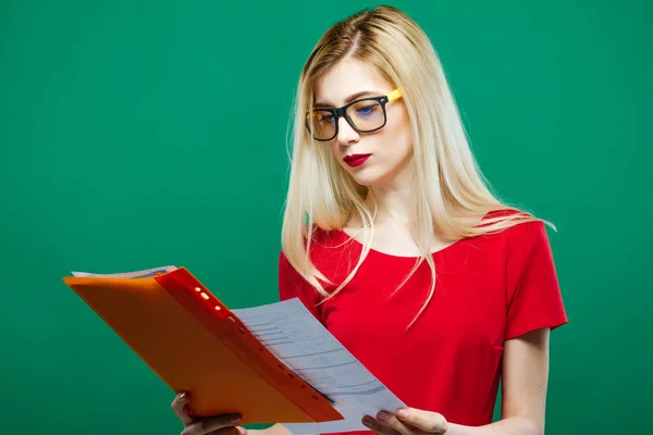 Studentessa intelligente in occhiali da vista e top rosso sta leggendo qualcosa su sfondo verde in Studio . — Foto Stock