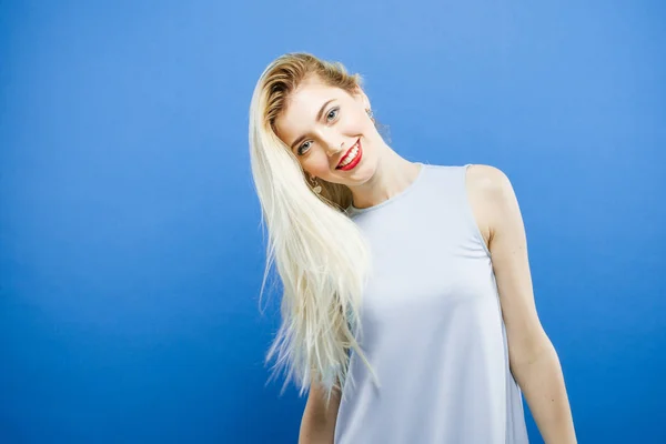 Attraente bionda con i capelli lunghi che indossa abito elegante è in posa su sfondo blu in Studio . — Foto Stock