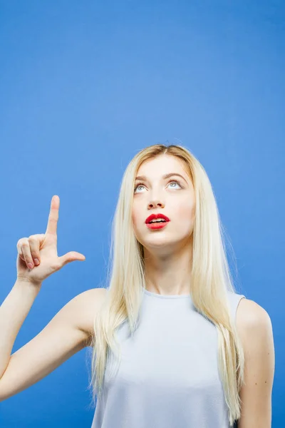 Sorprendida chica sobre fondo azul en estudio está apareciendo por su dedo . —  Fotos de Stock