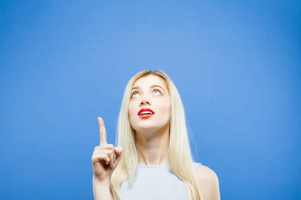 Atractiva rubia en vestido ligero está apareciendo por dedo. Studio Shot of Surprised Girl sobre fondo azul . —  Fotos de Stock