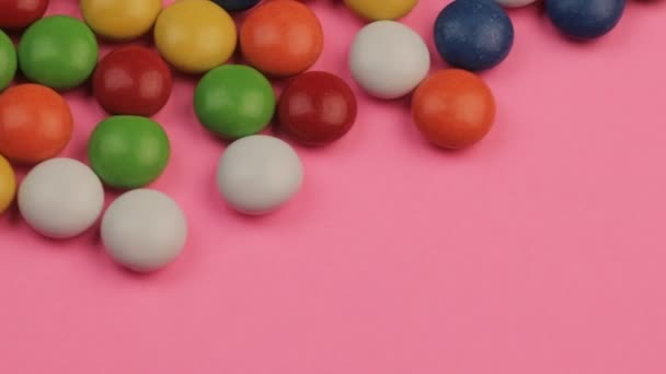 Primer plano de una pila de caramelos recubiertos de chocolate de colores sobre fondo rosa — Vídeos de Stock