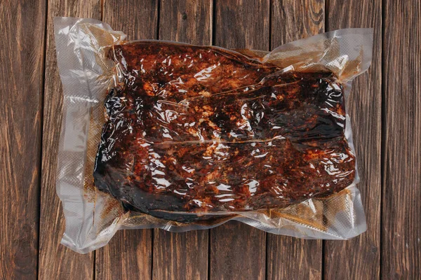 Salsiccia di maiale intera in un pacchetto sottovuoto su uno sfondo di legno. senza etichetta — Foto Stock