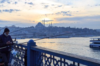 Istanbul 'da gün batımı sırasında Süleymaniye Camii arka planda Galata Köprüsü 'nde balıkçılık yapan insanlar