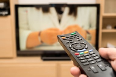 TV izlerken, siyah modern uzaktan kumanda kullanarak. TV uzaktan kumanda bir televizyon ile arka planda tutan el