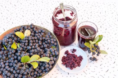 Taze meyve suyu ve cam ve berry tencerede beyaz dokulu arka plan üzerinde siyah chokeberry (Aronia melanocarpa) reçel
