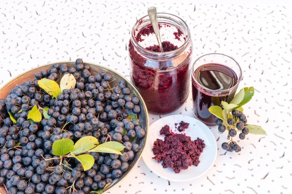 Jugo fresco y mermelada de chokeberry negro (Aronia melanocarpa) en vaso y baya en maceta sobre fondo blanco texturizado — Foto de Stock