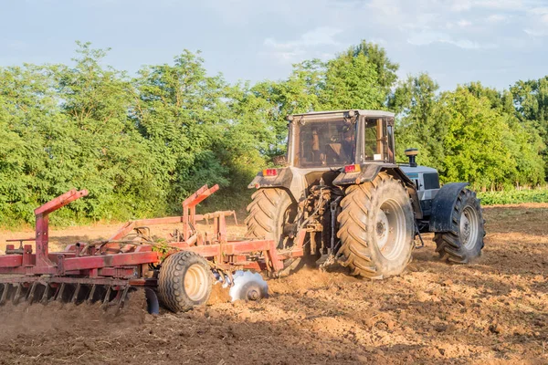 Big silver tractor with a red harrow (disc cultivator) in the field on a sunny day. The concept of work in a fields and agriculture industry. — Stock Photo, Image