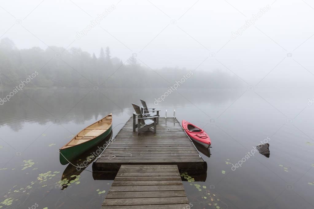 Canoe and kayak tied to a dock on a misty lake - Ontario, Canada