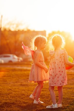 İki kız kardeş gün batımında bir top ve atlama halatıyla altın saatinde oyun bahçesinde oynuyorlar.