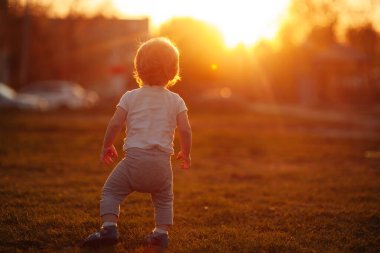 Çayırda küçük bir çocuk gün batımında gülümsüyor altın saatinde