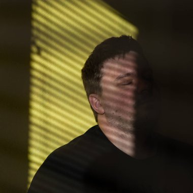 Sarı arka planda bir adamın portresi. Evdeki bir adamın portresi sarı bir duvarın arkasında. Perdelerin gölgesinde bir adamın görüntüsü