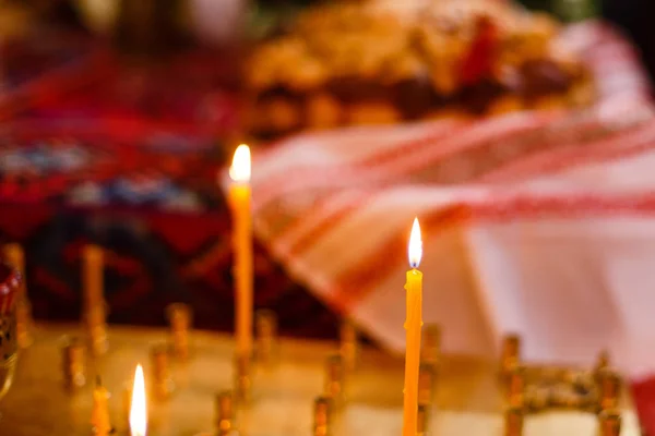 Single candle with dripping wax and blurring lights of many candles in two candlesticks at background. — Stock Photo, Image