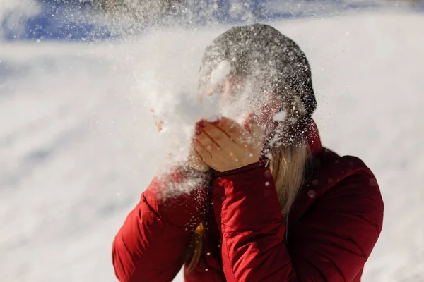 Bild von attraktiven Teenager-Mädchen weht Schnee auf ihren Handflächen, während das Tragen von Winterjacke mit Bokeh Hintergrund — Stockfoto