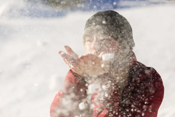 Bild von attraktiven Teenager-Mädchen weht Schnee auf ihren Handflächen, während das Tragen von Winterjacke mit Bokeh Hintergrund — Stockfoto