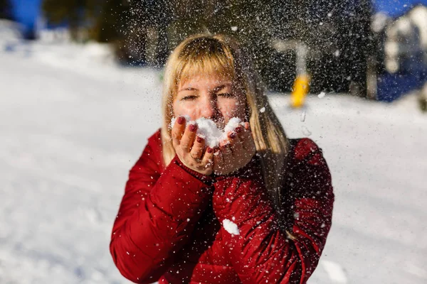 Bild von attraktiven Teenager-Mädchen weht Schnee auf ihren Handflächen, während das Tragen von Winterjacke mit Bokeh Hintergrund — Stockfoto