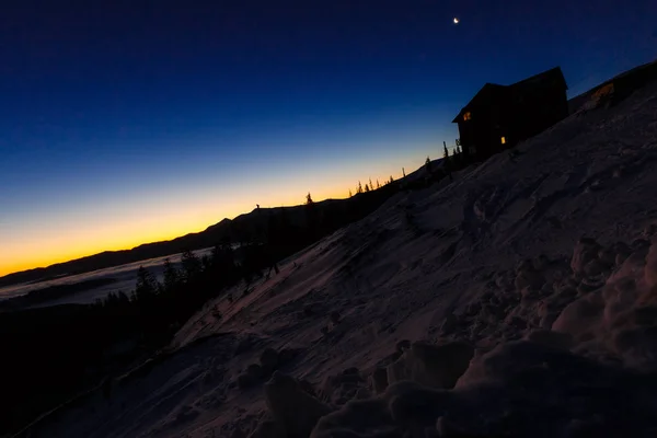 Casa de madera con una luz en la ventana. Paisaje nocturno en invierno —  Fotos de Stock