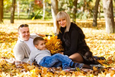 Anne, baba ve oğul akçaağaç yapraklarında oynuyorlar.