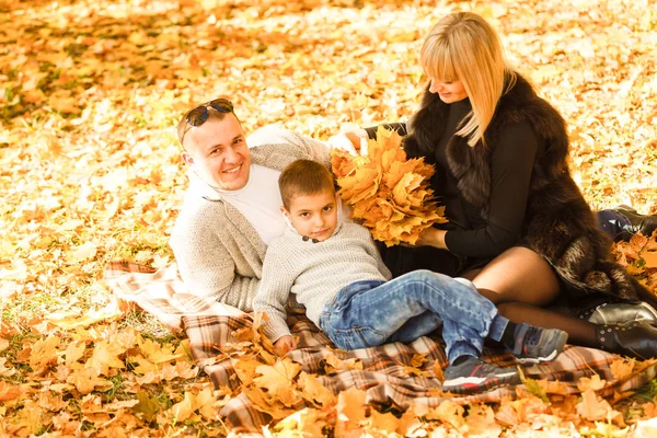 ママとパパと息子はカエデの葉の山で遊ぶ — ストック写真