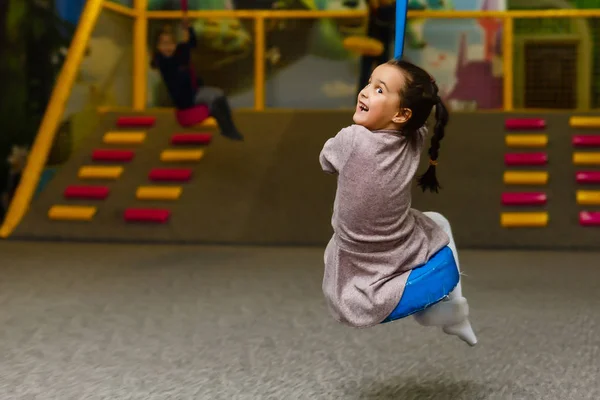 Linda niña está jugando en el patio de recreo. La chica está montando — Foto de Stock