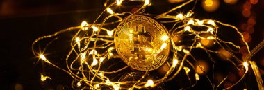 Altın Bitcoin parası. Neşeli bir atmosfer. Arka planda renkli Noel ağacı ışıkları var. Btc bir kripto para birimidir ve paylaşımcı ödeme şebekesinin merkezden uzaklaşmış ilk ağıdır..