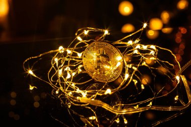 Altın Bitcoin parası. Neşeli bir atmosfer. Arka planda renkli Noel ağacı ışıkları var. Btc bir kripto para birimidir ve paylaşımcı ödeme şebekesinin merkezden uzaklaşmış ilk ağıdır..