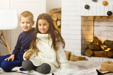 Noel arifesinde aile şöminede. Noel ağacının altında hediye kutularıyla çocuklar. Geleneksel şöminesi olan dekore edilmiş oturma odası. Evde sıcak bir kış akşamı.. 