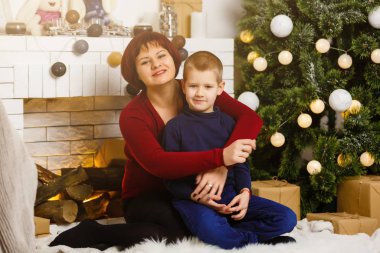 Oturma odasında şöminesi ve Noel ağacı olan anne ve oğlu Noel hediyesi hazırlıyorlar. 