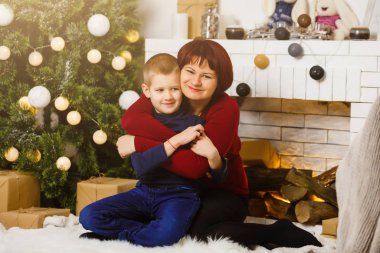 Oturma odasında şöminesi ve Noel ağacı olan anne ve oğlu Noel hediyesi hazırlıyorlar. 