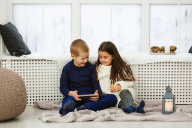 İki küçük çocuk oturuyor: Tablet bilgisayarı ve telefonu olan bir kız.