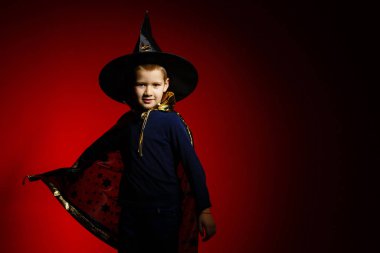 Kırmızı arka planda büyücü gibi giyinmiş bir çocuk. 