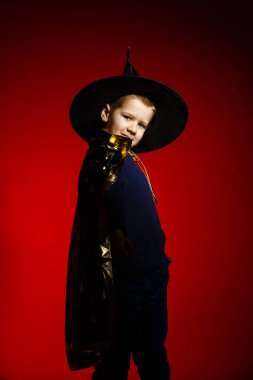 Kırmızı arka planda büyücü gibi giyinmiş bir çocuk. 