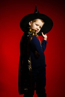 Kırmızı arka planda büyücü gibi giyinmiş bir çocuk. 