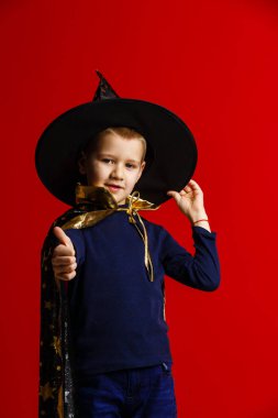 Kırmızı arka planda büyücü gibi giyinmiş bir çocuk. 