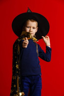 Kırmızı arka planda büyücü gibi giyinmiş bir çocuk. 