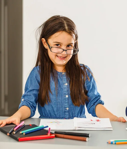 Menina escrevendo algo no livro e sentado à mesa — Fotografia de Stock