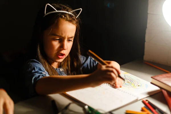 Дівчина-підліток з ноутбуком робить домашнє завдання за столом ввечері — стокове фото