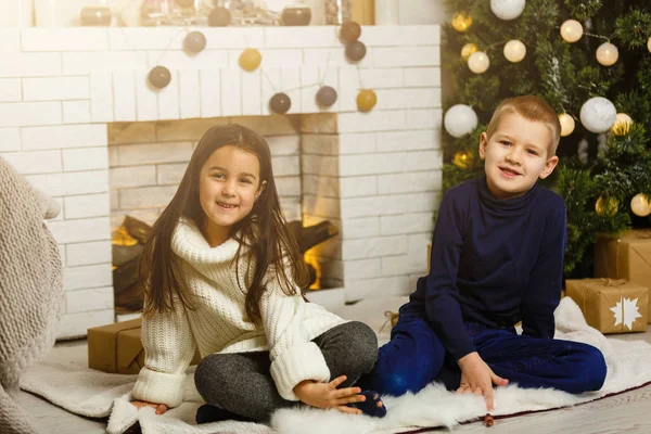 Family on Christmas eve at fireplace. Children under Christmas tree with gift boxes. Decorated living room with traditional fire place. Cozy warm winter evening at home.