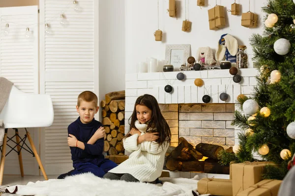 Family on Christmas eve at fireplace. Children under Christmas tree with gift boxes. Decorated living room with traditional fire place. Cozy warm winter evening at home.