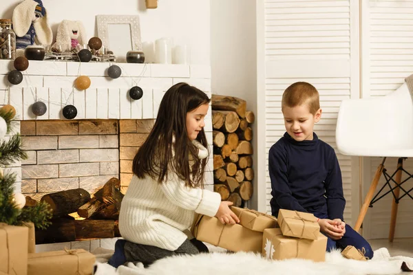 Family on Christmas eve at fireplace. Children under Christmas tree with gift boxes. Decorated living room with traditional fire place. Cozy warm winter evening at home.