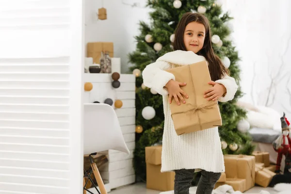 Ein kleines Weihnachtsmädchen öffnet ein Weihnachtsgeschenk und ist überrascht — Stockfoto