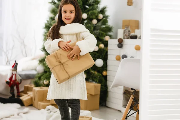 Una piccola ragazza di Natale apre un regalo di Natale ed è sorpresa — Foto Stock