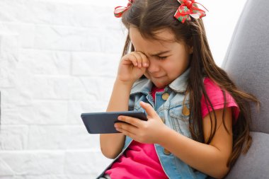 Küçük kız ağlıyor ve akıllı telefon tutarak. Küçük kız yüzünü sakladı ve ağladım, bir cep telefonu onun elinde tutan.