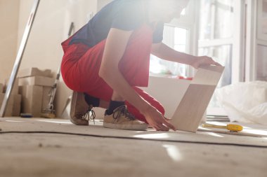 Üstad iş kıyafetleri giyiyor, fayans döşemeyi kontrol ediyor, bina seviyesini kullanıyor, ayarlamalar yapıyor, profesyonel onarım işi yapıyor. 