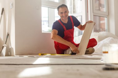 Üstad iş kıyafetleri giyiyor, fayans döşemeyi kontrol ediyor, bina seviyesini kullanıyor, ayarlamalar yapıyor, profesyonel onarım işi yapıyor. 