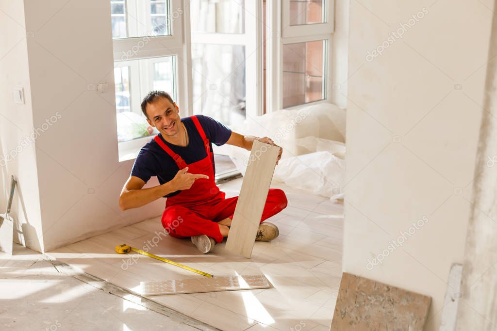 Master is wearing work clothes, is checking horizon of installing tiles, using building level, adjusting, professional repairing work 