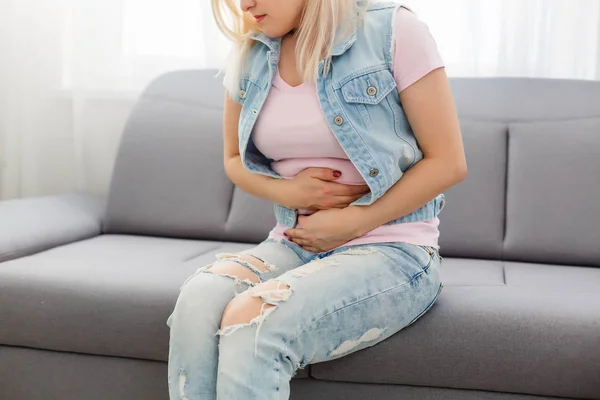期間を持つアジアの女の子はソファの上に座っていると彼女の胃の上に痛みを感じる 女性の痛みや月経症候群と呼ばれています 彼女は胃の上に保持し 痙攣を通してカール — ストック写真