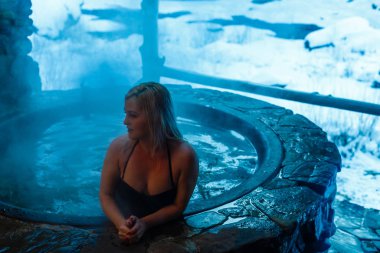 Genç bir kadın dağlarda küvette dinleniyor.