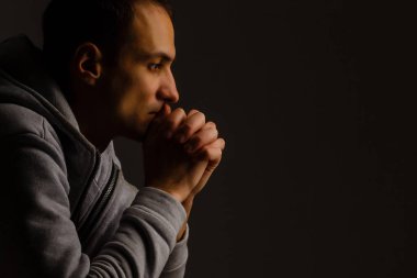 Religious young man praying to God on dark background, black and