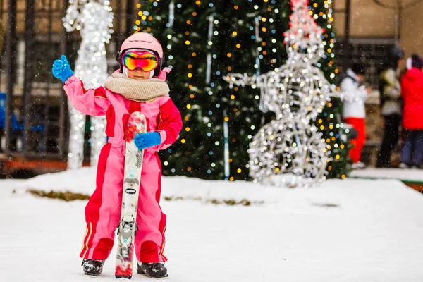 小女孩带着护目镜和头盔参加寒假 站在户外滑雪板后面看着相机 微笑着兴奋的特写模糊的背景 — 图库照片